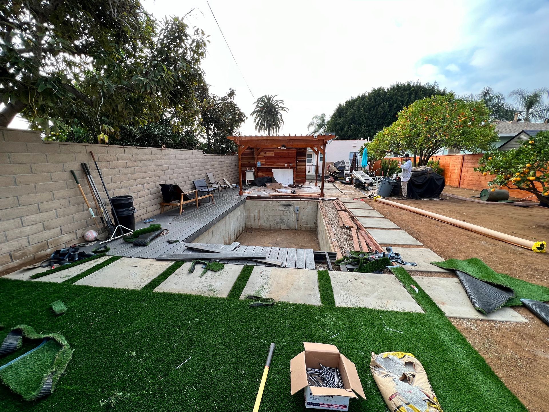 Backyard with a large excavated pool under construction, pavers, artificial grass, and building materials