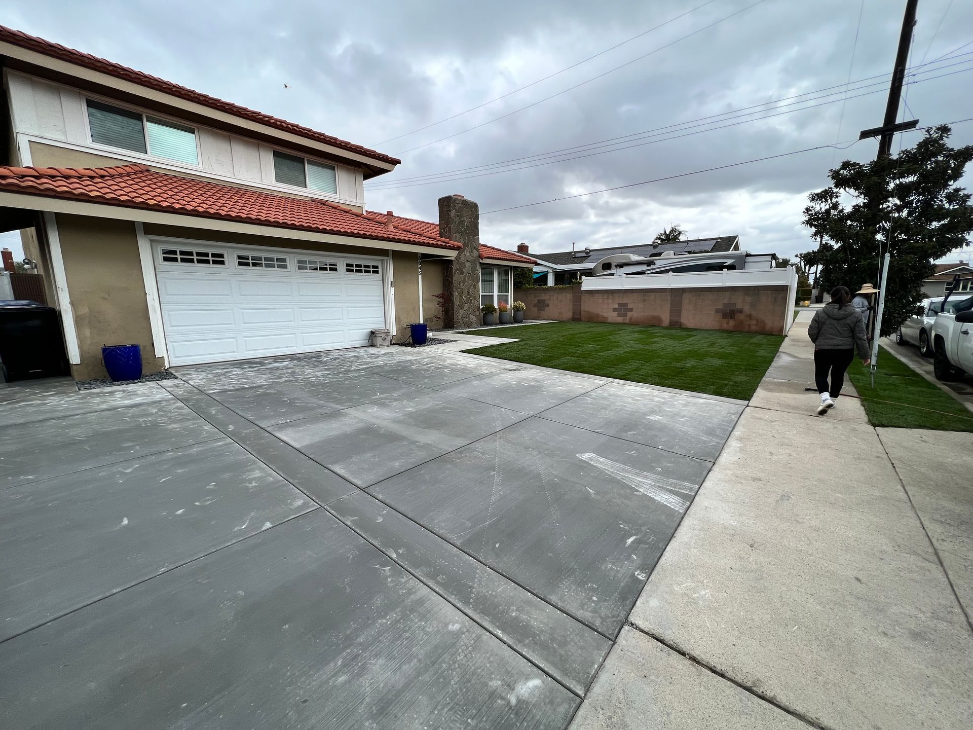 Suburban house with a white garage door, concrete driveway, and a person walking on the sidewalk