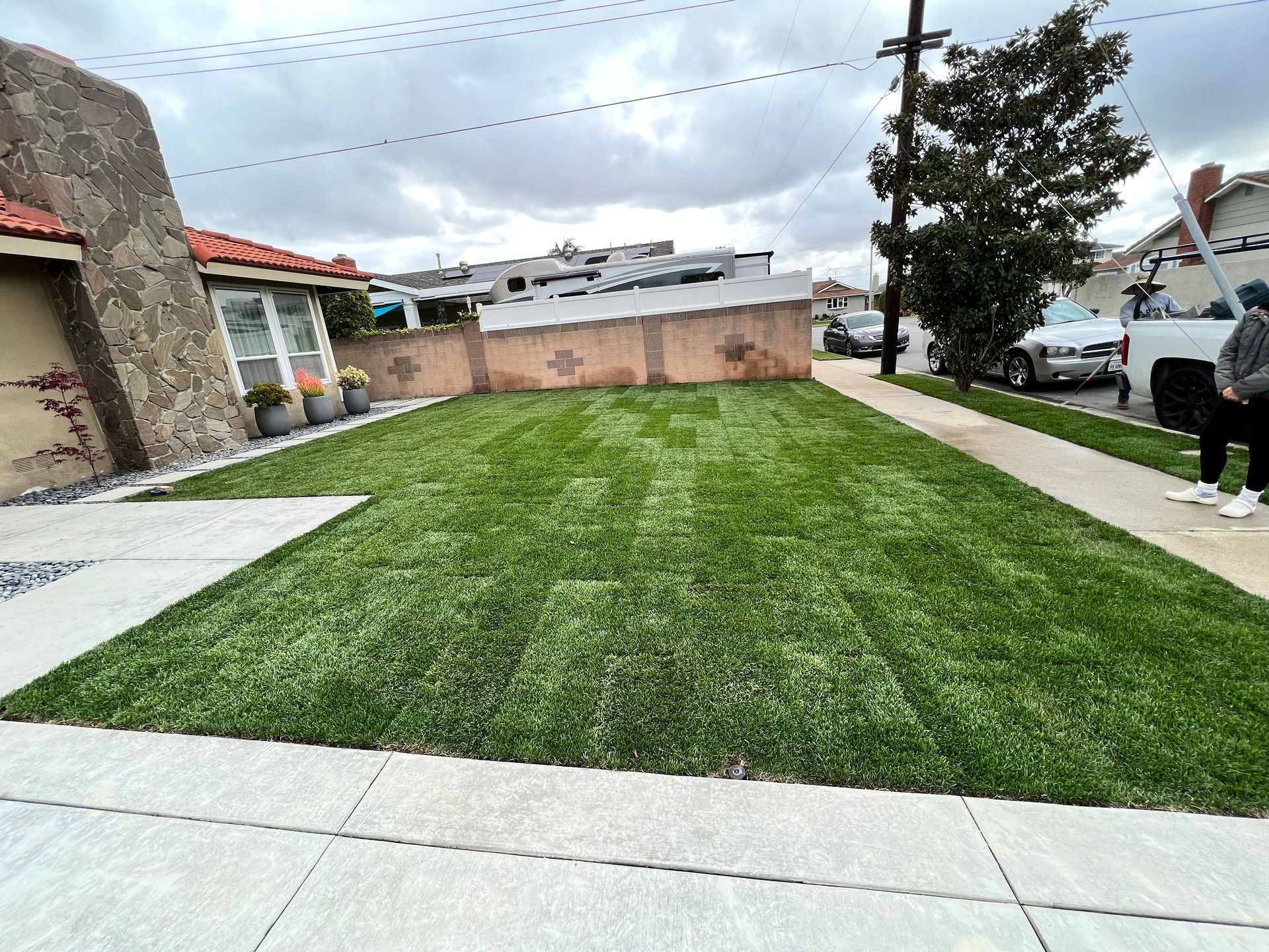 Grassy backyard patio with stone paths, a tree, and a parked white truck by a brick wall.