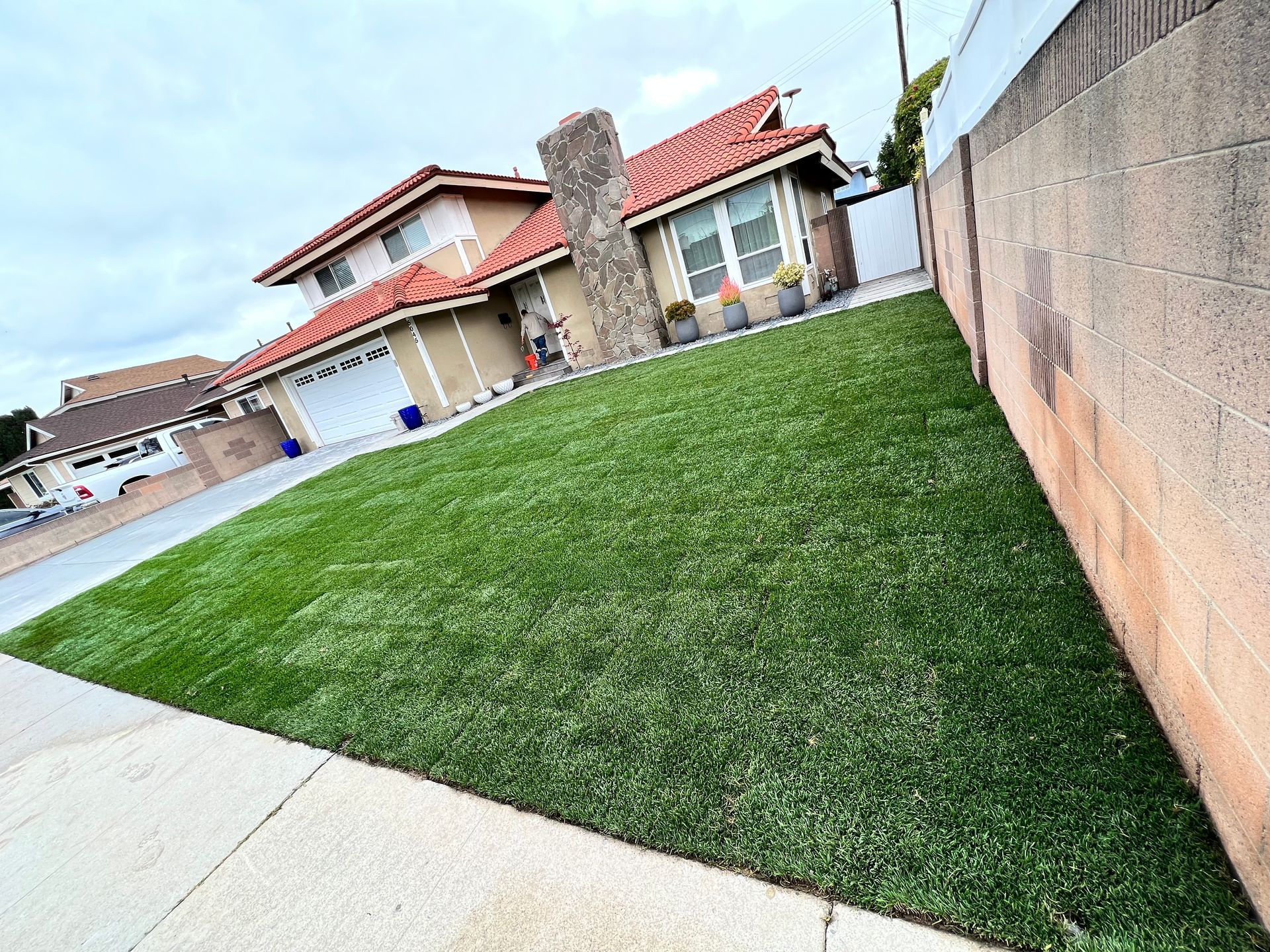 Suburban house with a green lawn and driveway beside a concrete wall.