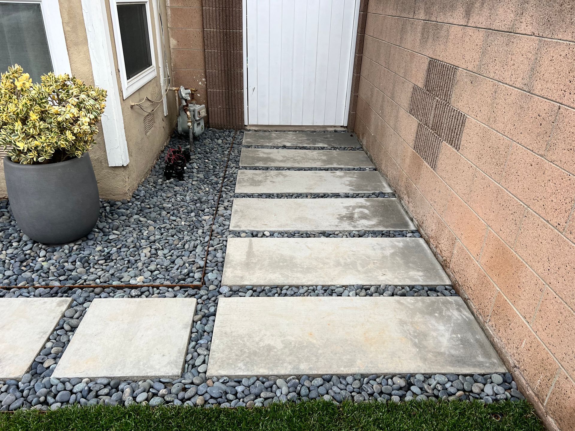 Stone walkway with stepping slabs and gravel beside a house, leading to a white door and wall.