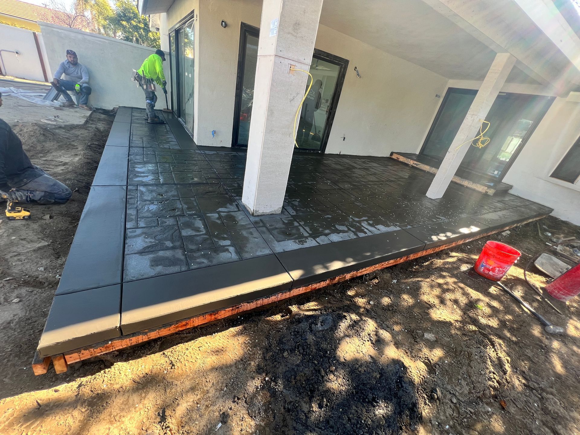 Patio under construction with wet concrete, white columns, and two workers in high-visibility clothing