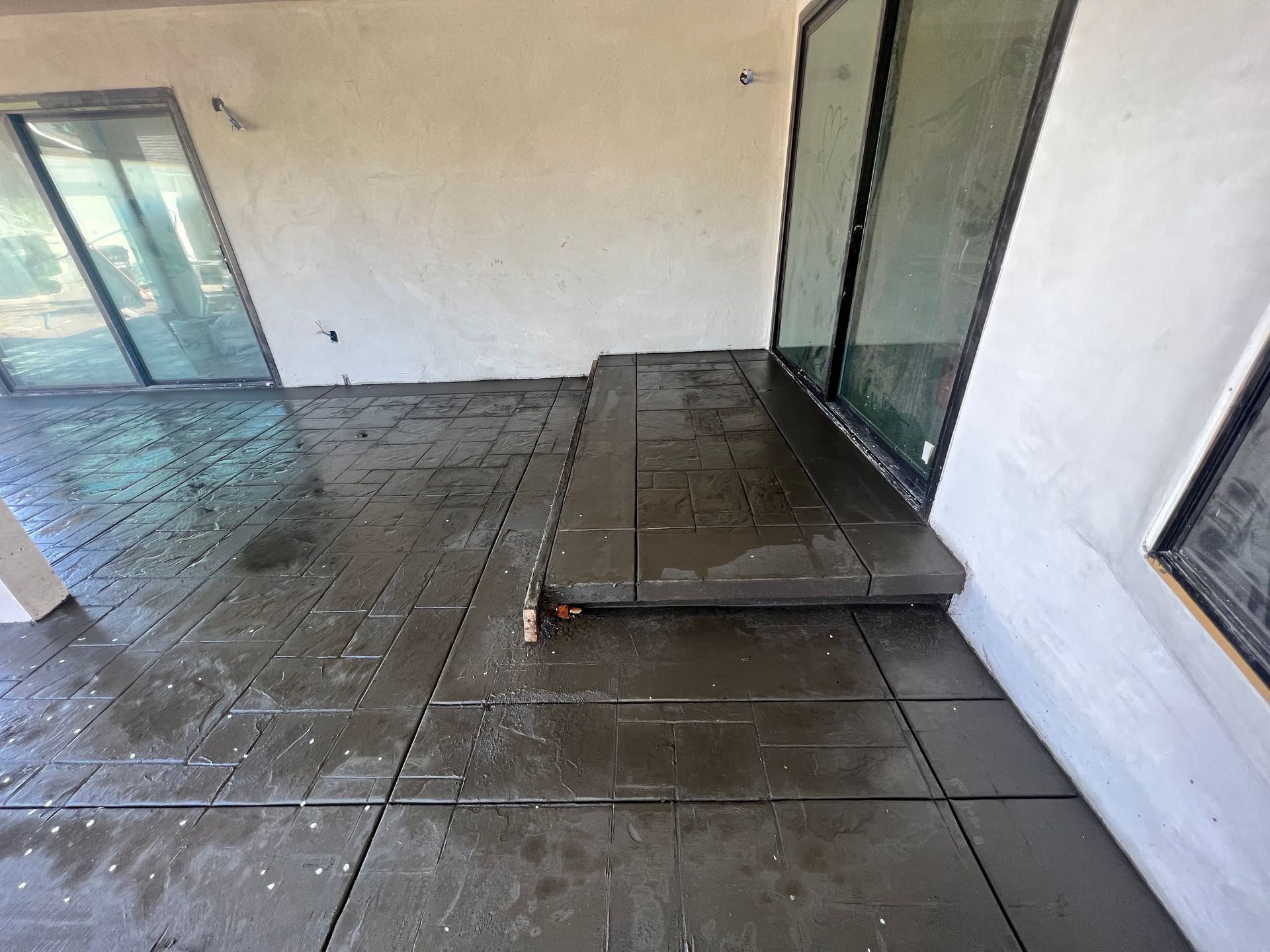 Patio with wet tile flooring and a low platform beside sliding glass doors, viewed from an angle.
