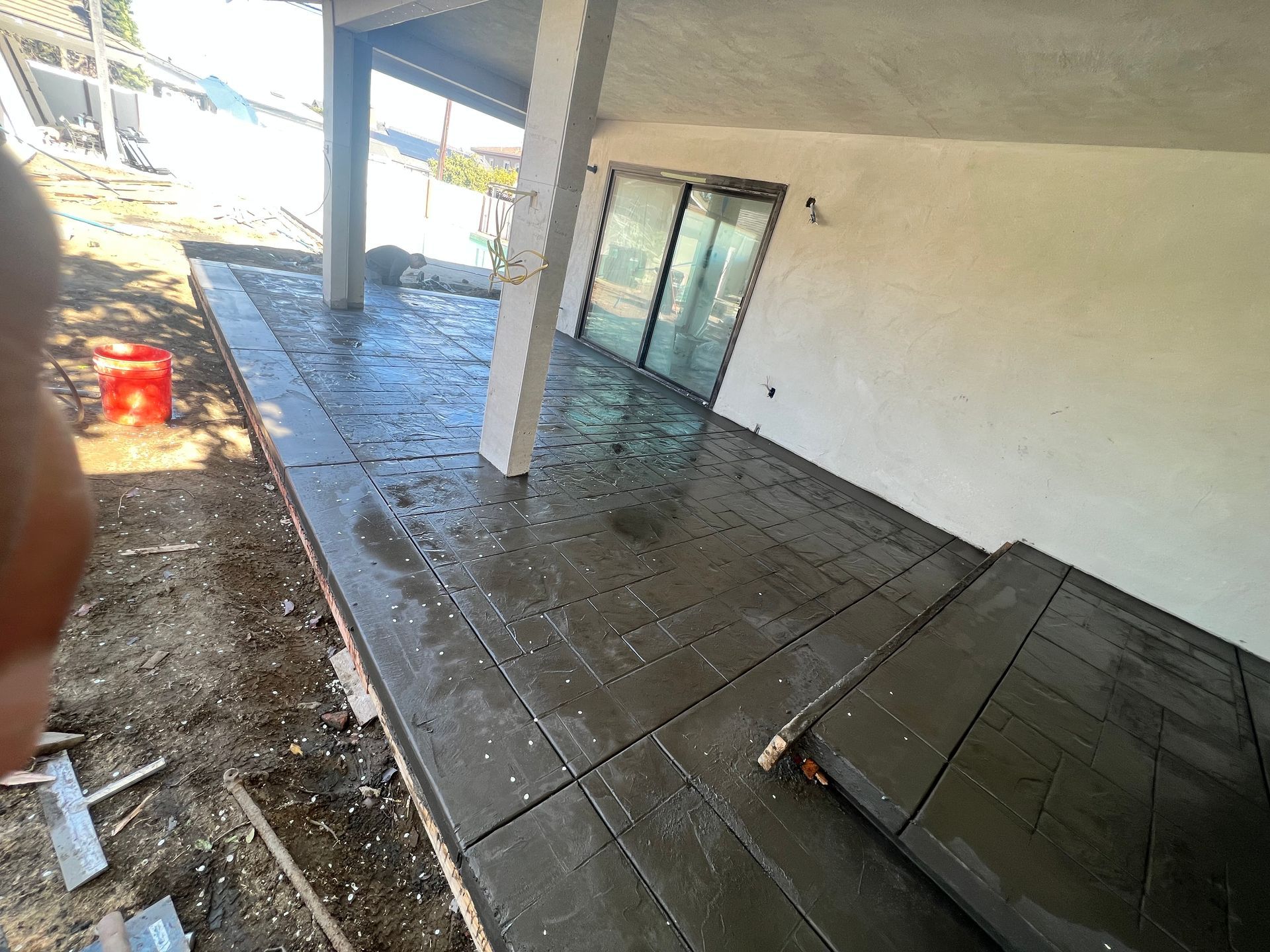 Concrete patio under a covered porch with a glass door and construction debris on the left.