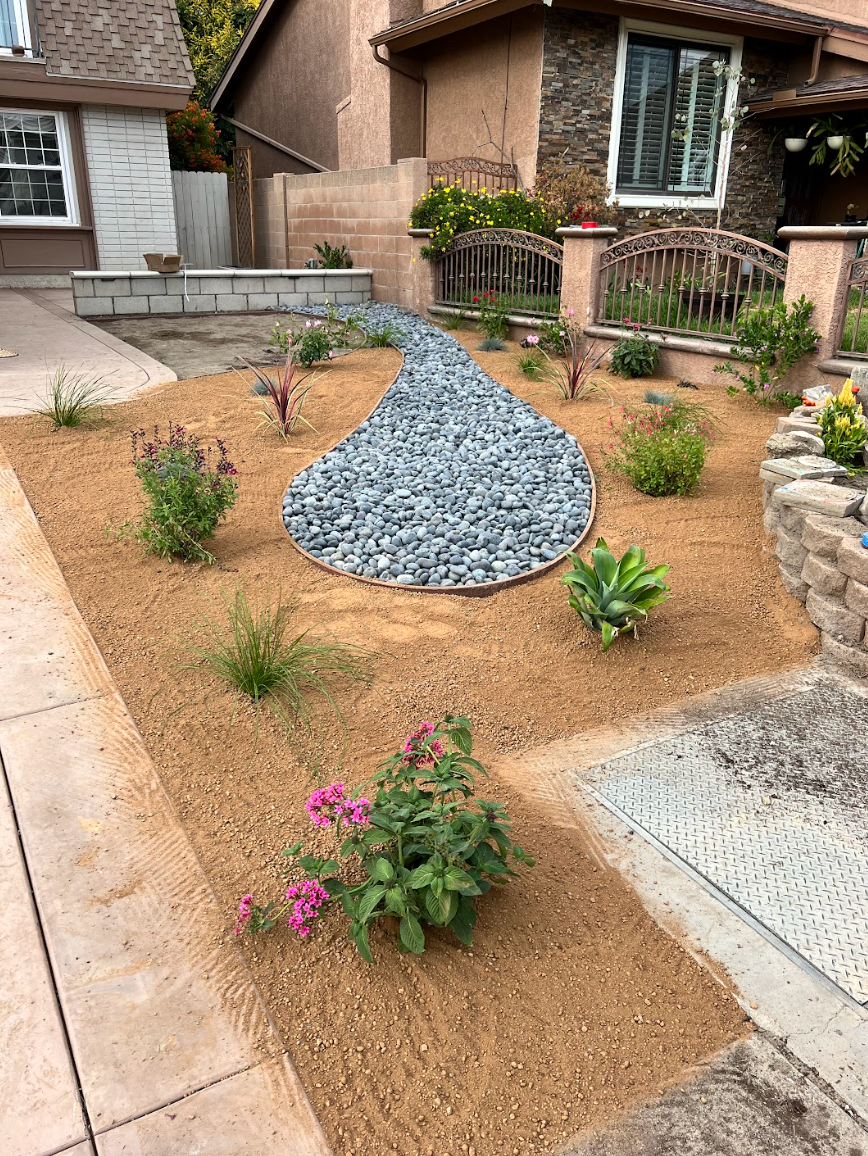 Front yard xeriscape with gravel mound, small plants, and stone steps beside a brick house