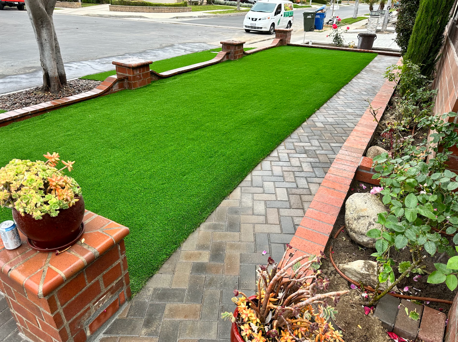 Neatly landscaped front yard with bright green grass, brick edging, and a stone path beside a street.