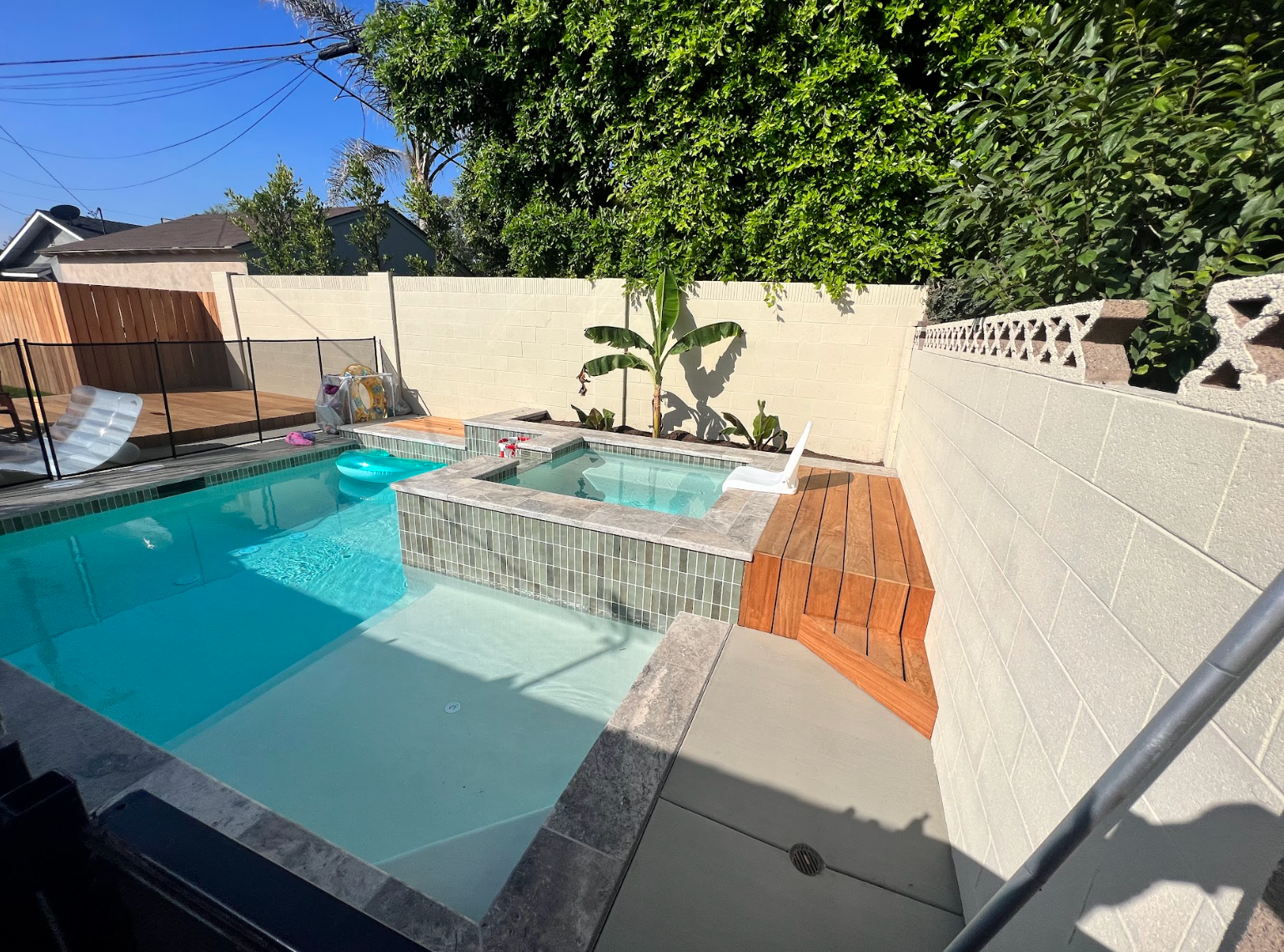 Backyard swimming pool with raised spa, tan walls, and bright blue water in sunlight