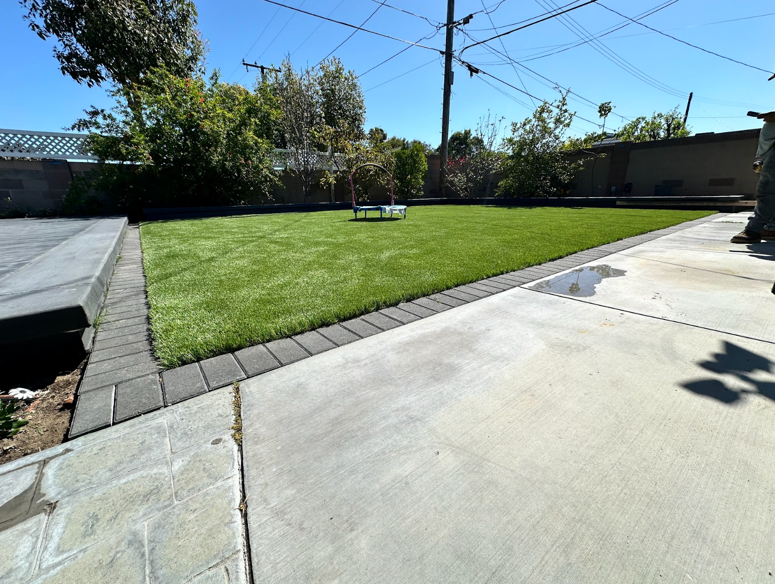 Backyard with green lawn, concrete patio, and a bench under a blue sky