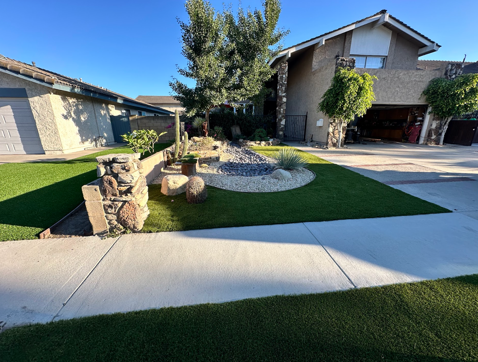 Suburban front yard with stone garden feature, curved lawn, and driveway beside a two-story house