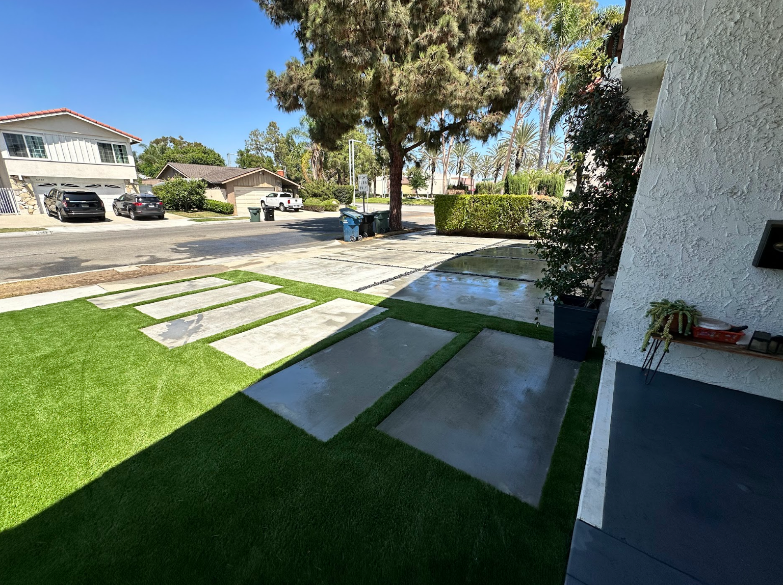 Front yard with stepping stones, green lawn, and driveway beside a house on a sunny day