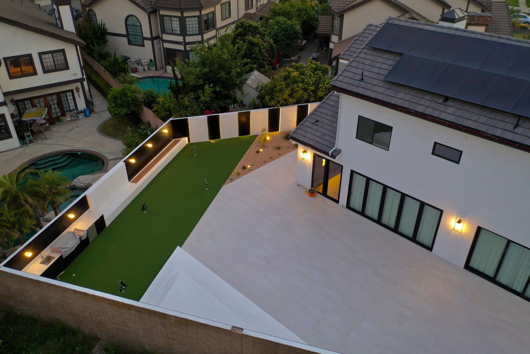 Overhead view of a modern courtyard with green turf, paved patio, and lit building at dusk