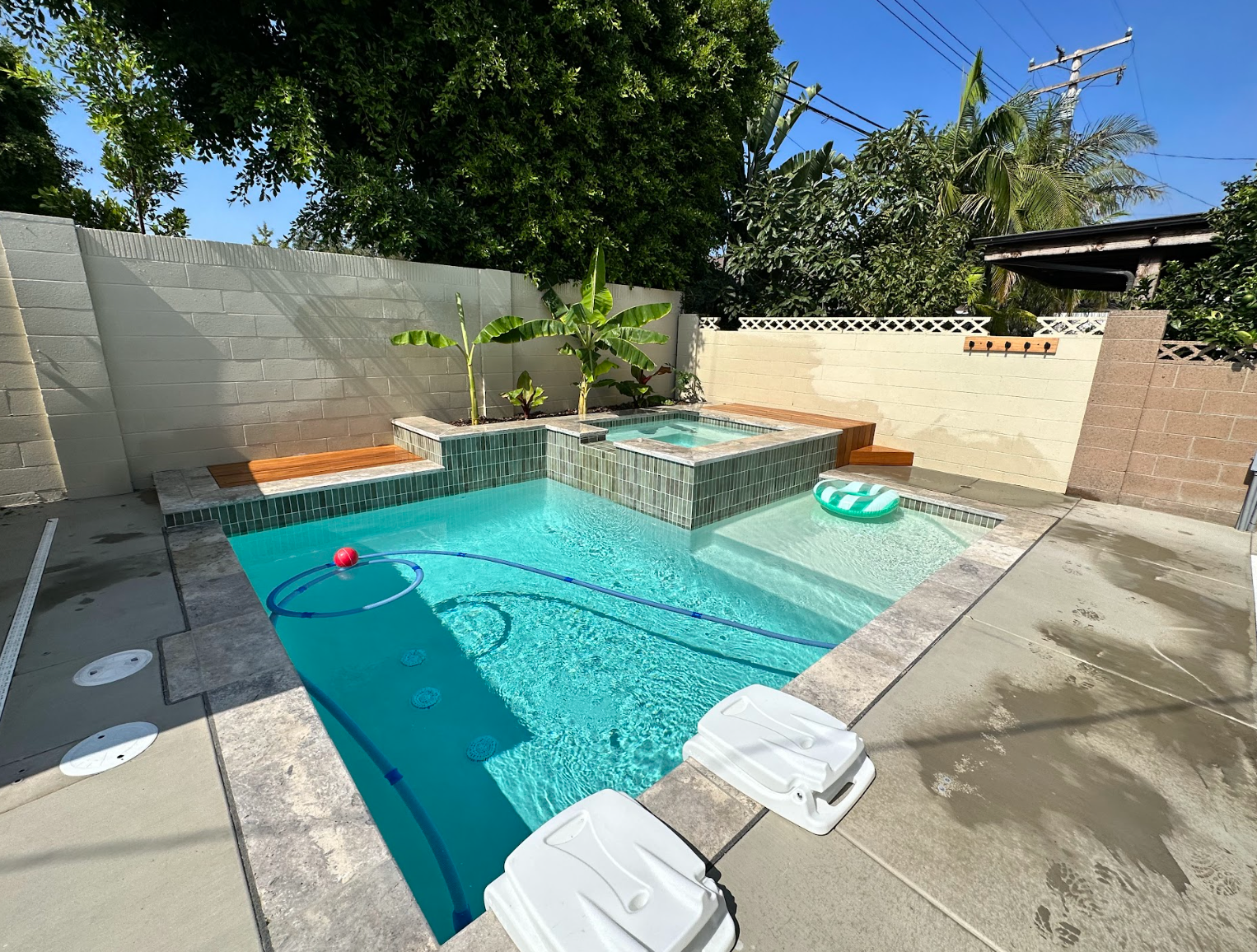 Small backyard pool with turquoise water, stone patio, and lounge floats beside a raised spa and wall fountain.