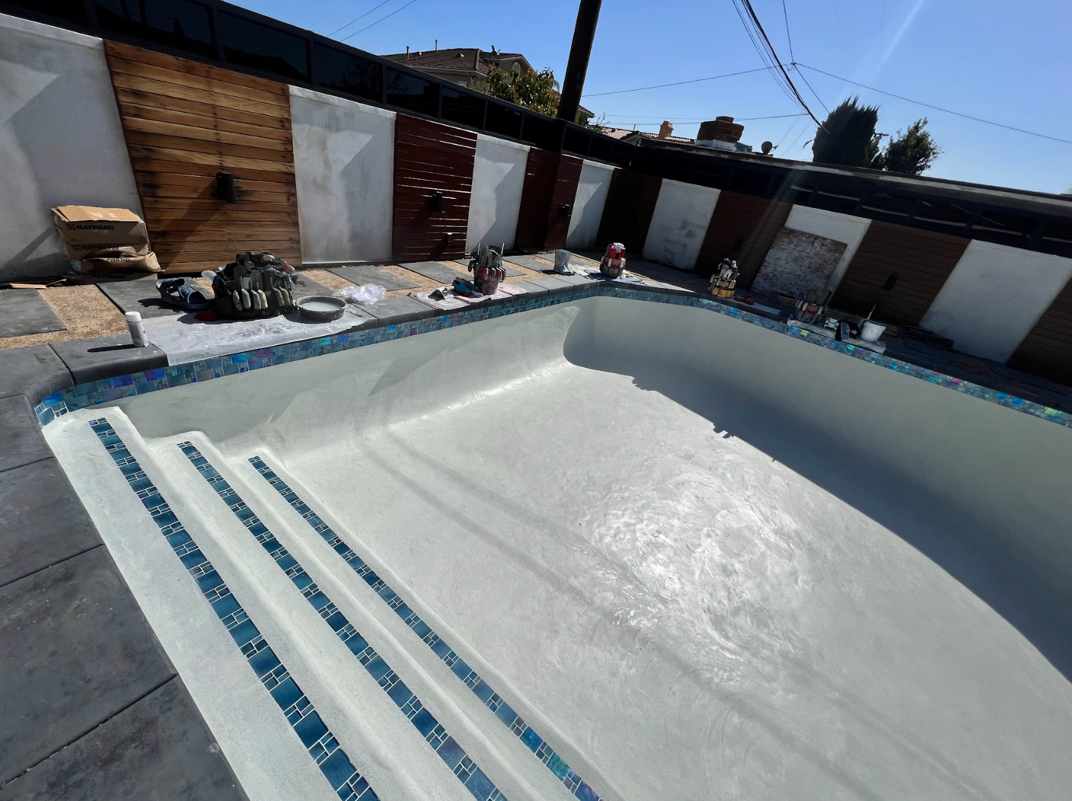 Empty backyard swimming pool under repair, with blue steps and a partially finished white interior.