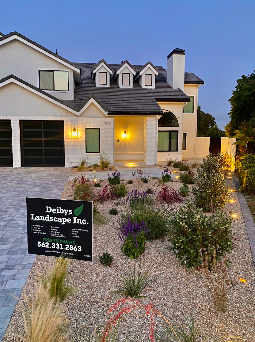 Two-story white house with lit windows and a sign for Daisy’s Transcription Inc. in the front yard at dusk