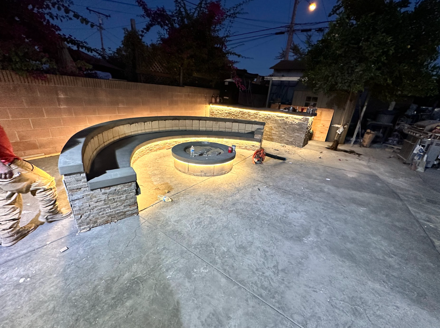 Curved stone bench around a lit fire pit in an outdoor patio at dusk
