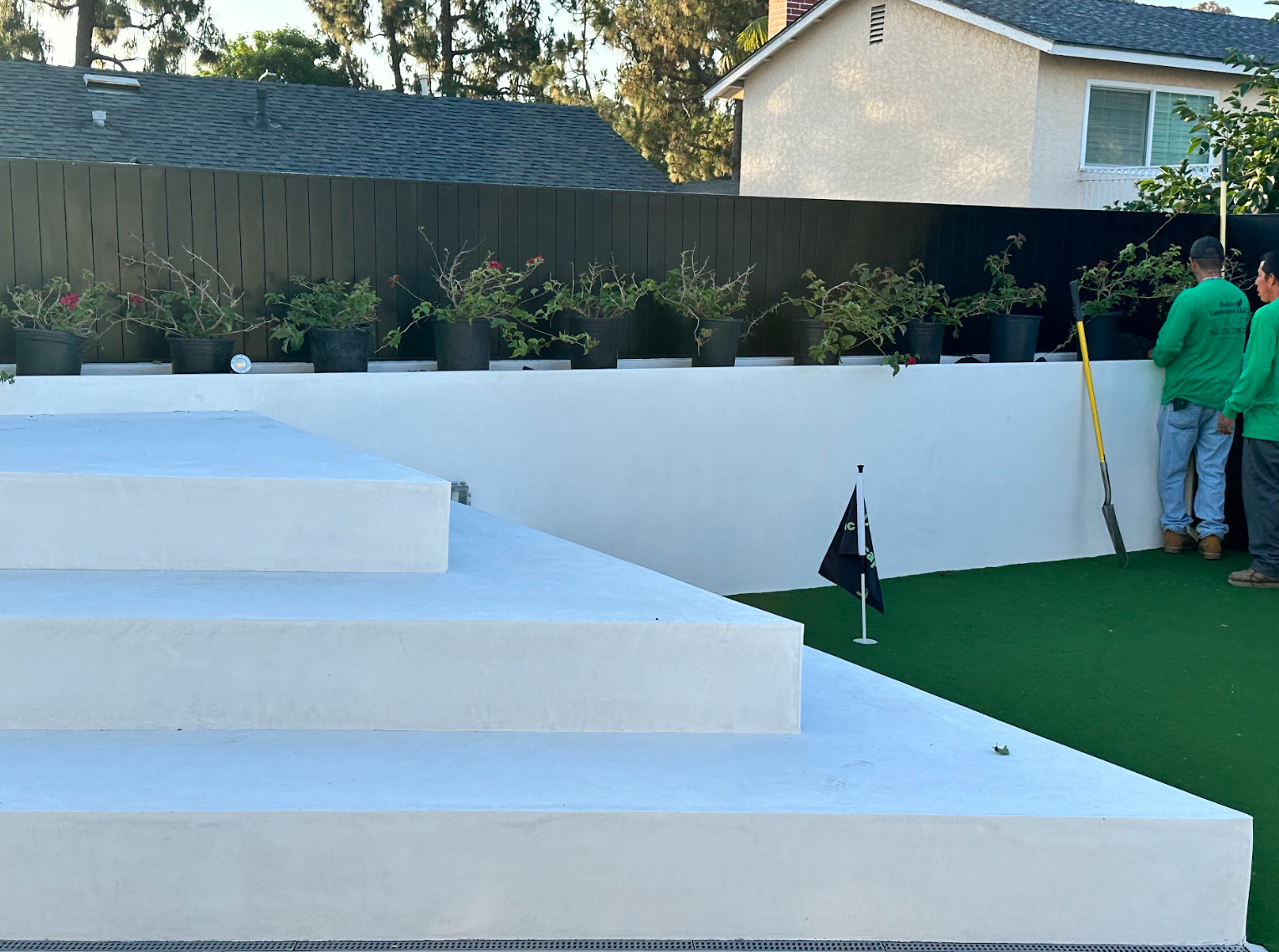 White outdoor steps beside a green artificial-turf area, with two people near a white wall and fence.