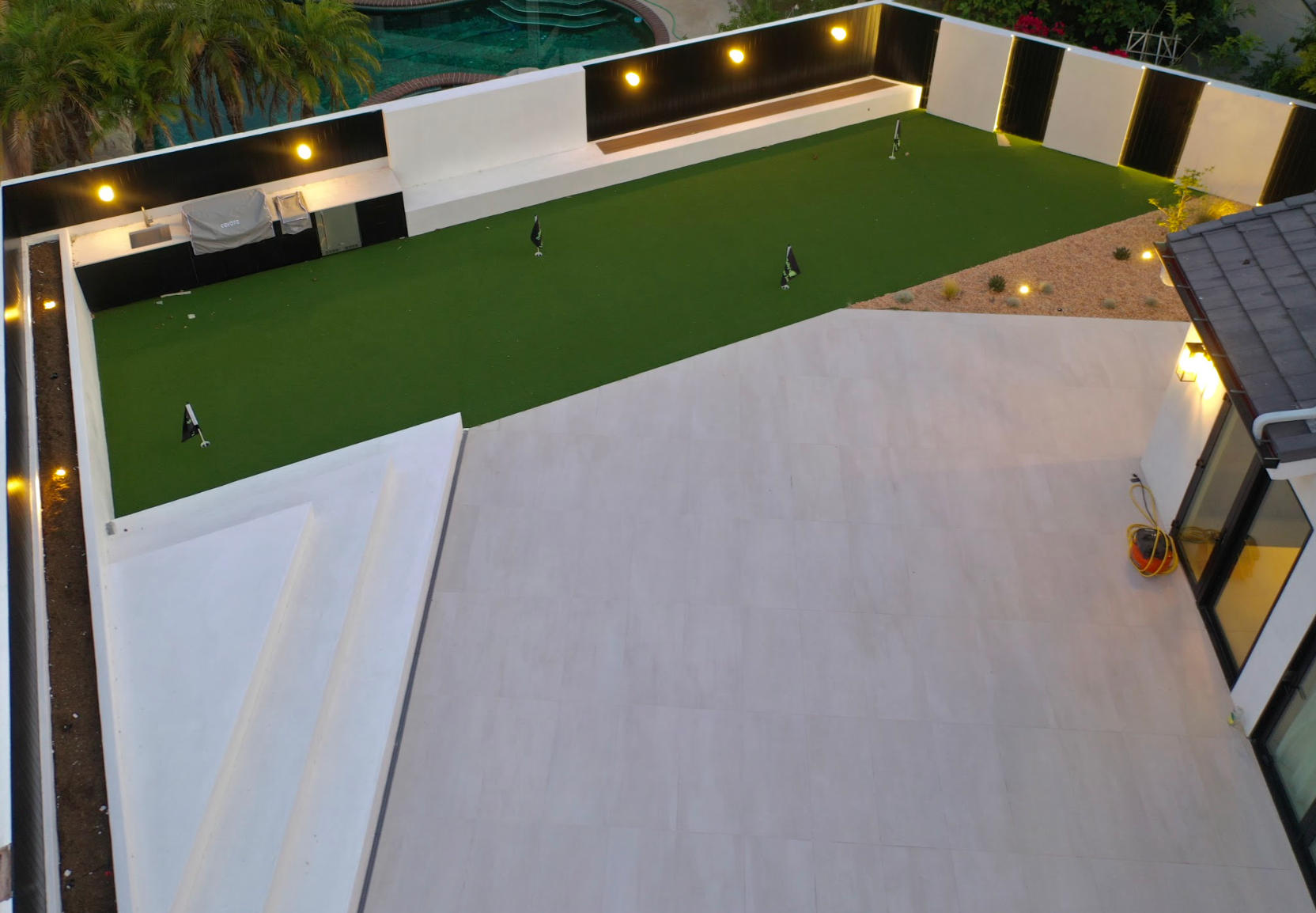 Courtyard with artificial turf, white patio, and modern black-and-white walls lit by warm lights