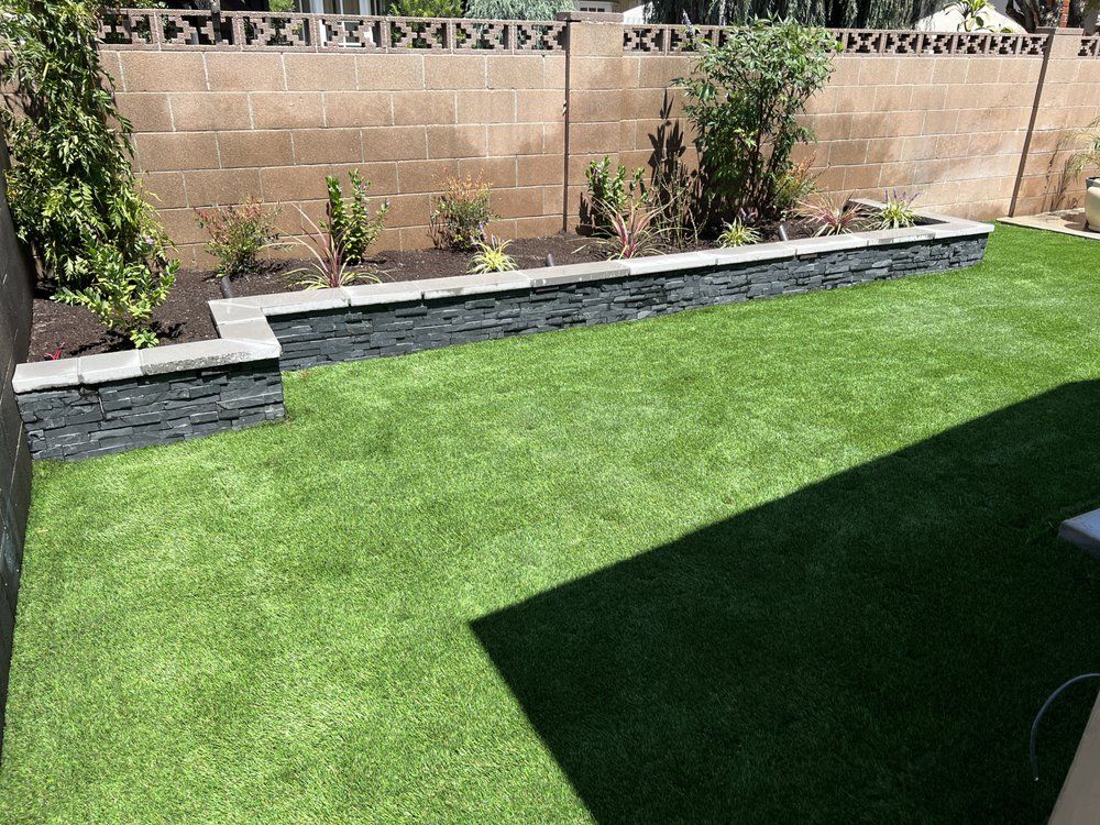 Backyard with green lawn, raised stone planter, and brick wall along the fence line.
