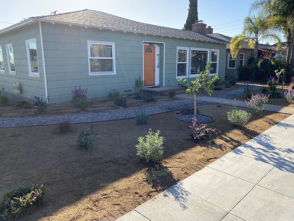 Single-story house with gray siding, orange front door, and dry front yard landscaping along a sidewalk