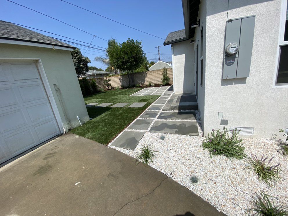 Side yard walkway with concrete path, white gravel, garage door, and white house exterior under a clear blue sky