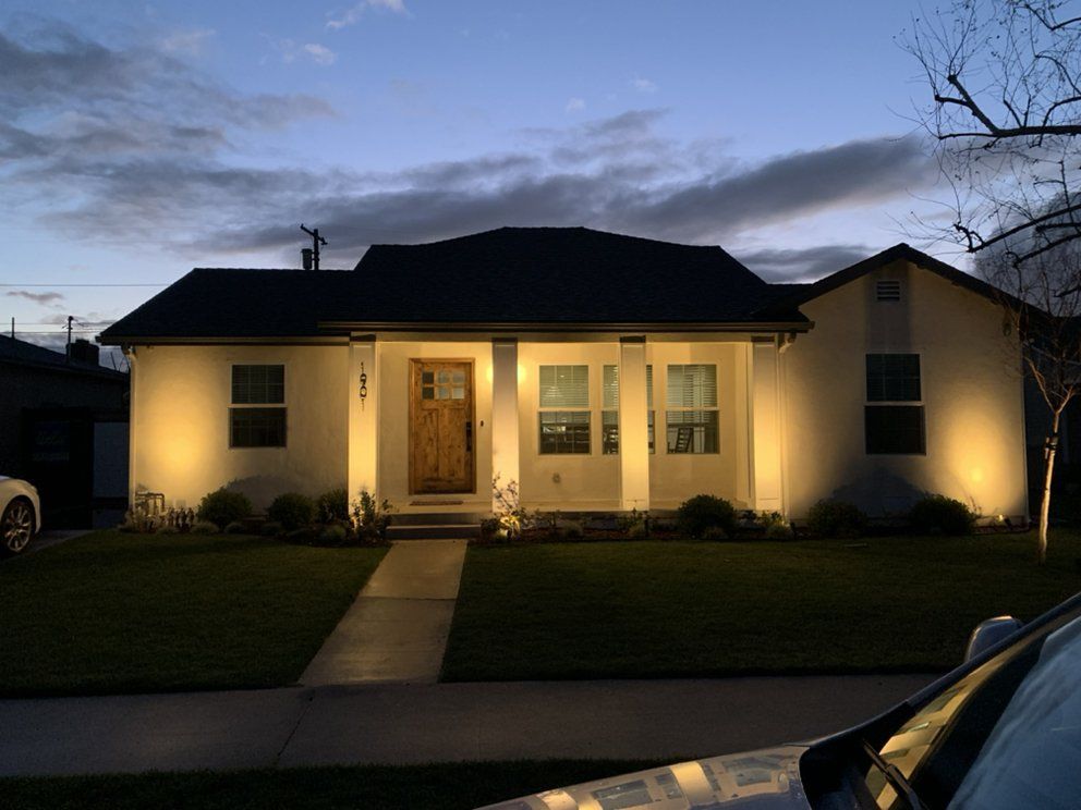 Single-story house lit warmly at dusk, with a front walkway and dark sky overhead