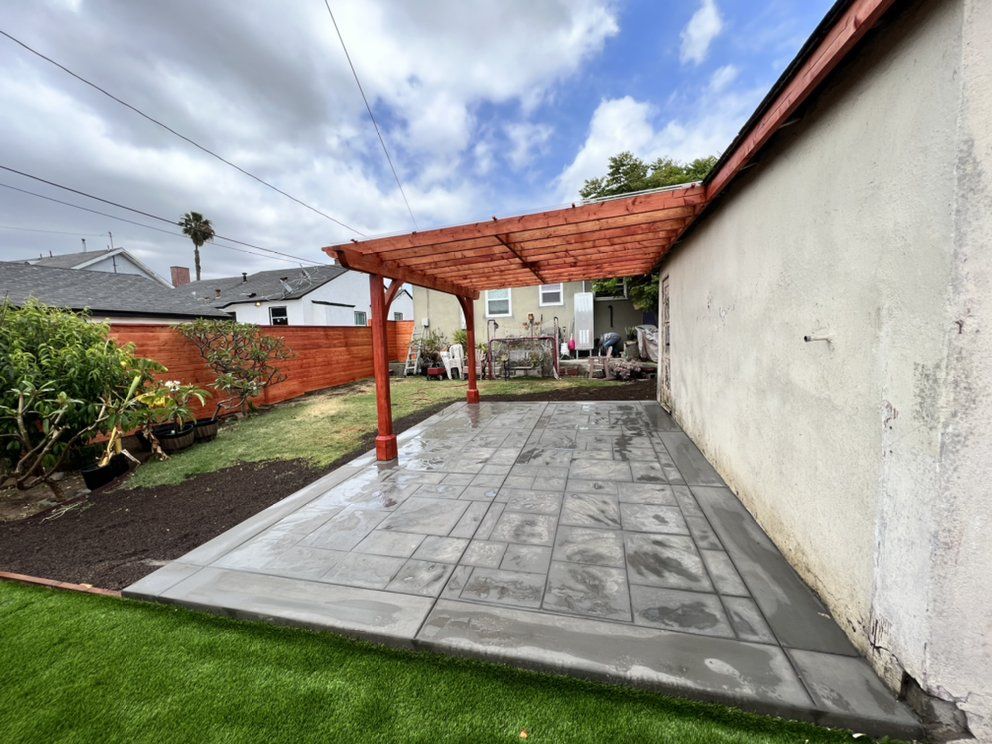 Covered patio with gray tile flooring, white wall, red brick pillars, and a grassy yard under cloudy sky
