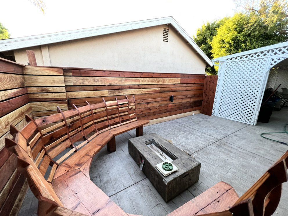 Curved wooden bench around a concrete fire pit on a backyard patio with a white lattice screen