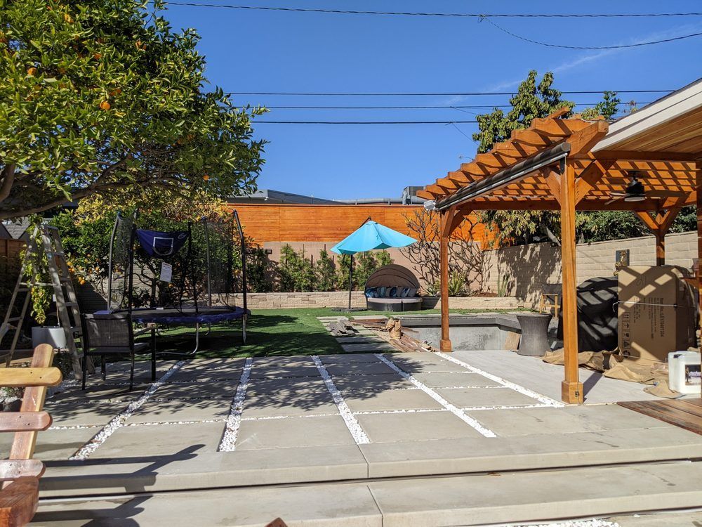 Backyard patio with pergola, trampoline, umbrella, and concrete court under clear blue sky