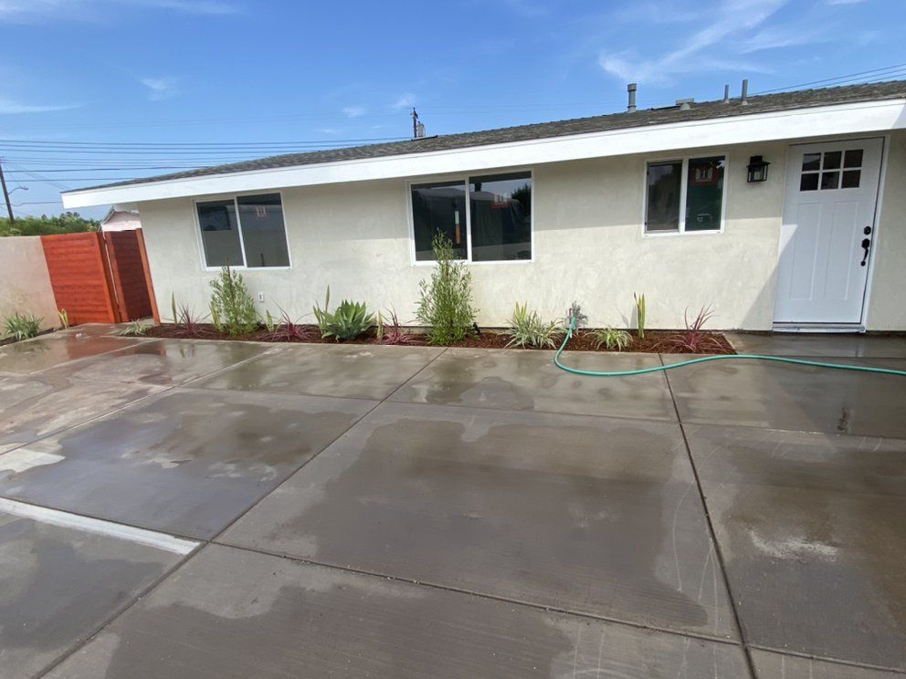 Single-story white house with a wet concrete driveway and front walkway under a blue sky