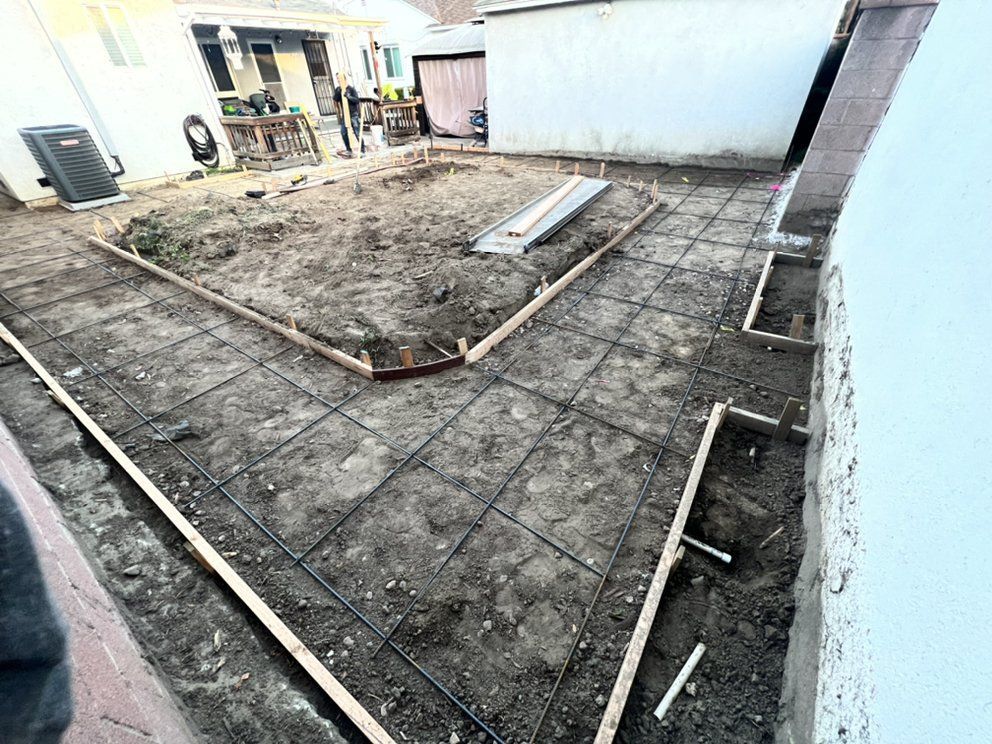 Construction site with rebar grid and wooden forms for a concrete slab in a courtyard.