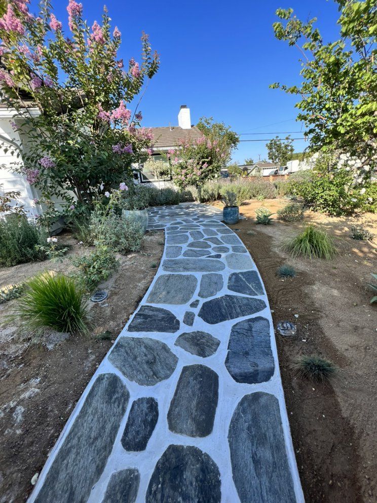 Stone garden path through a landscaped yard with pink flowers and blue sky