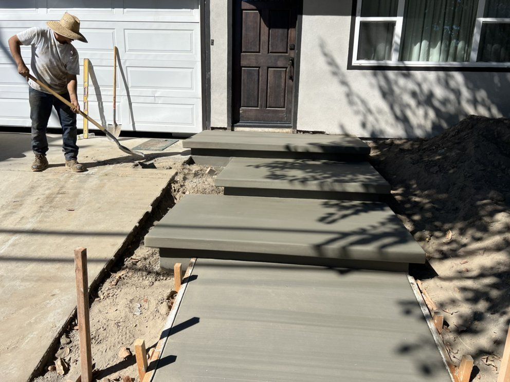 Worker smoothing wet concrete walkway beside a house entrance and garage