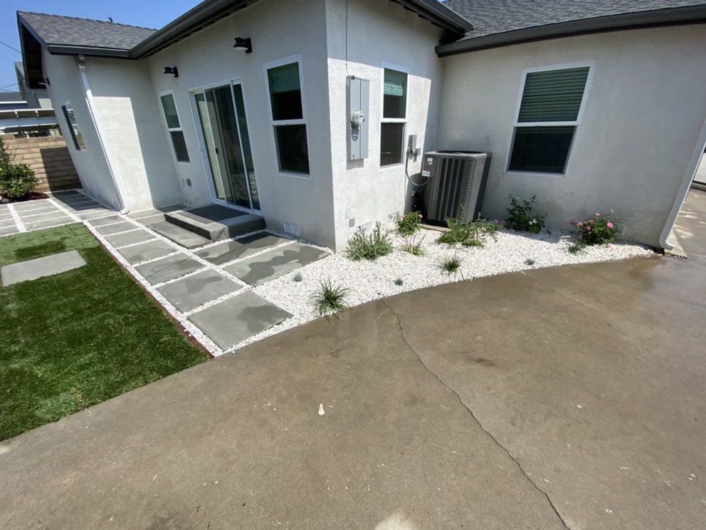 Front of a white house with a concrete driveway, stone walkway, and small lawn under sunny skies