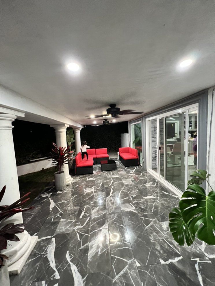 Covered patio with glossy marble floor, red lounge chairs, ceiling fan, and glass sliding doors at night