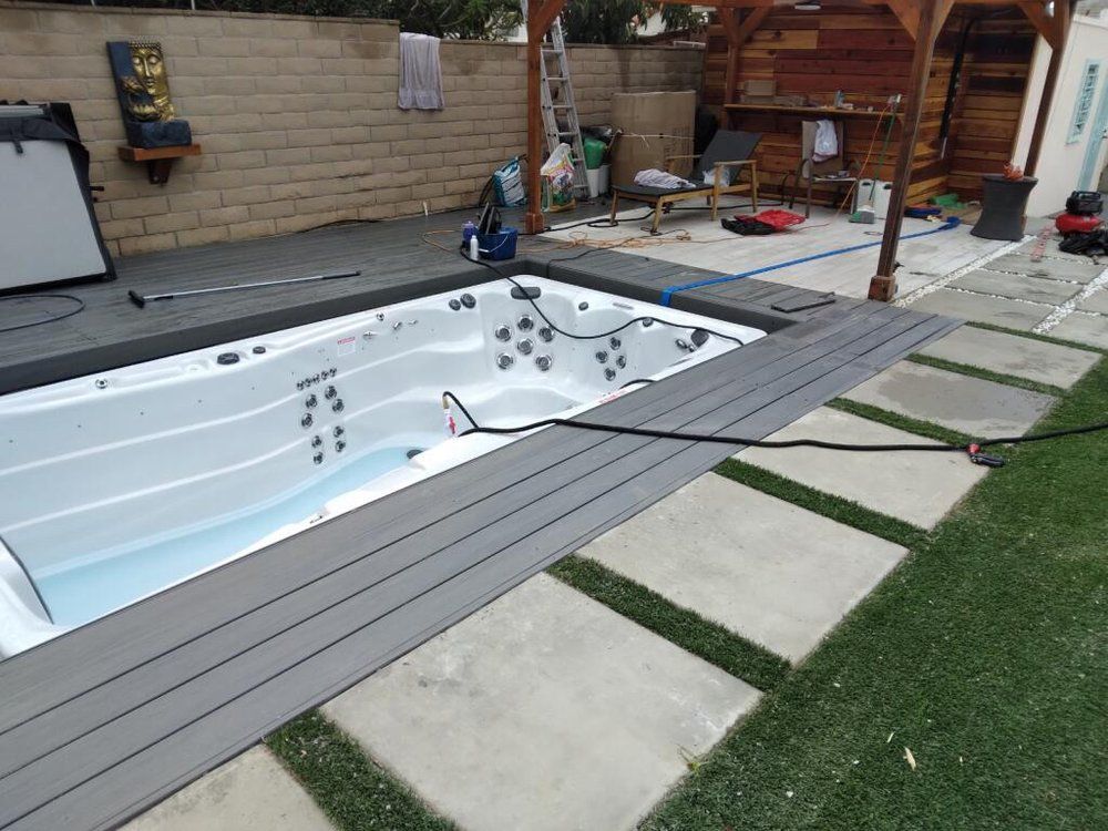 Backyard pool being installed, with gray deck boards and scattered tools beside a brick wall