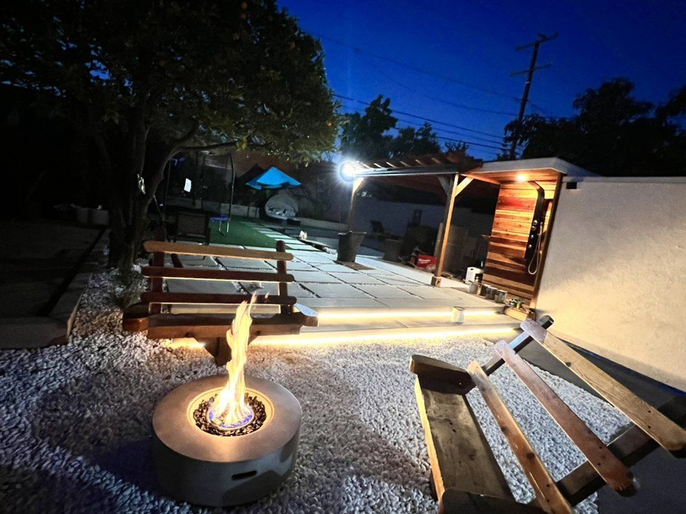 Outdoor patio at night with a fire pit, benches, string lights, and a lit poolside cabana