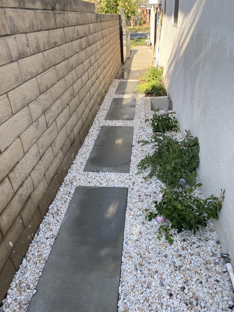 Narrow side yard with concrete stepping stones, white gravel, and a stucco wall beside a block wall