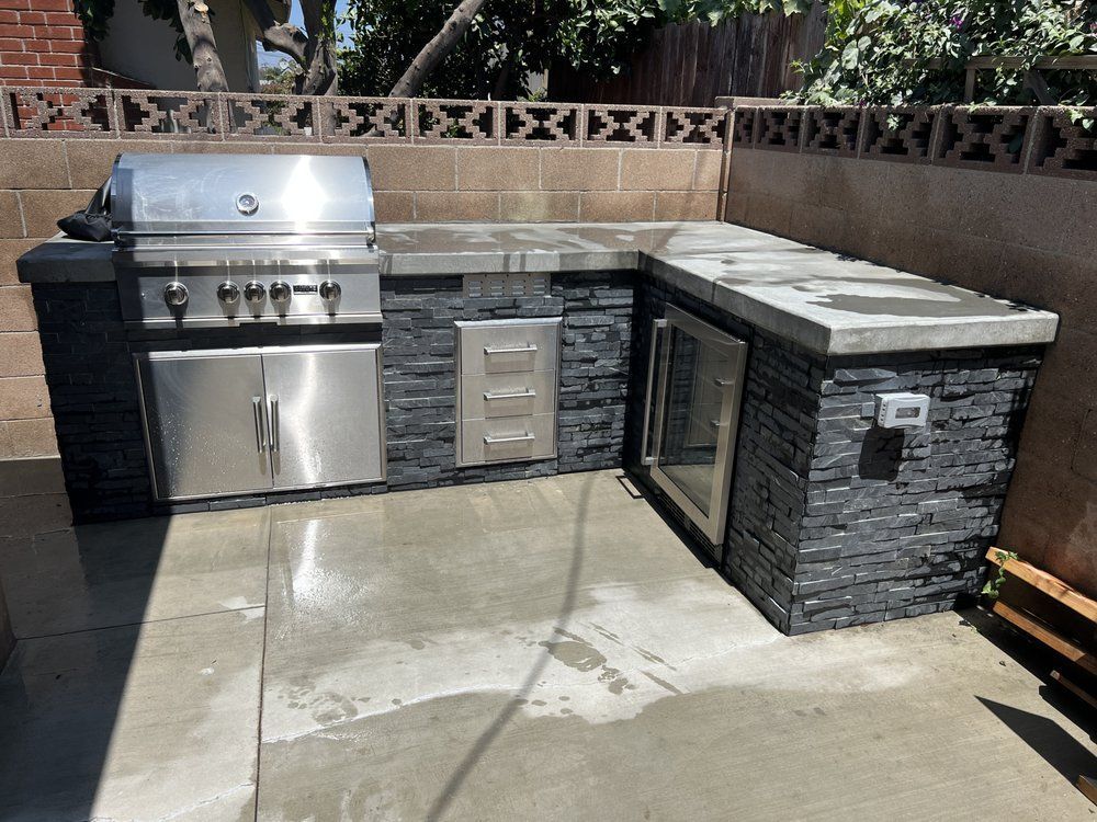 Outdoor patio with built-in stainless steel grill, sink, and stone countertop island.