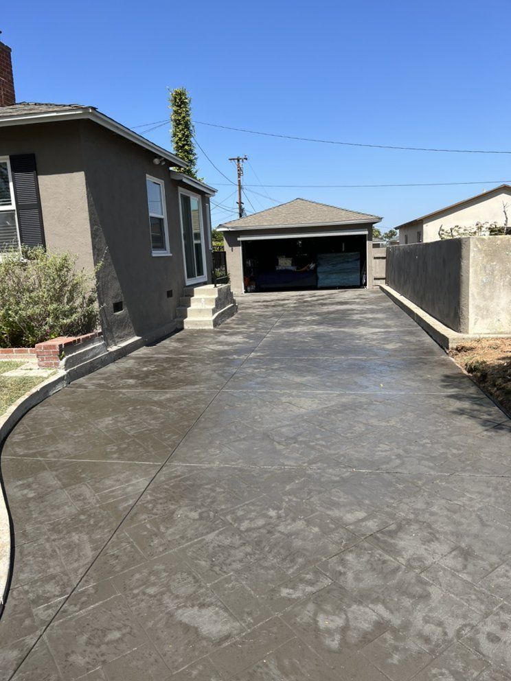 Concrete driveway leading to a garage beside a gray house on a sunny day