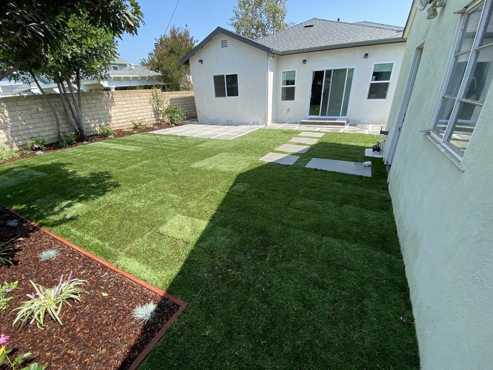 Backyard with green lawn, stone pavers, and a light-colored house with sliding glass doors.