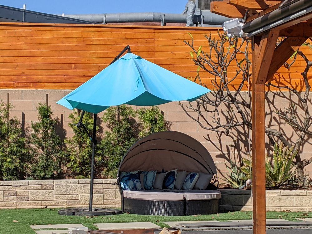 Backyard daybed with blue umbrella beside a wooden fence and pergola