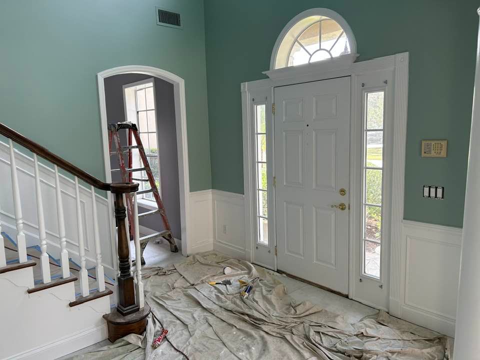 A hallway with stairs and a ladder in it is being painted.