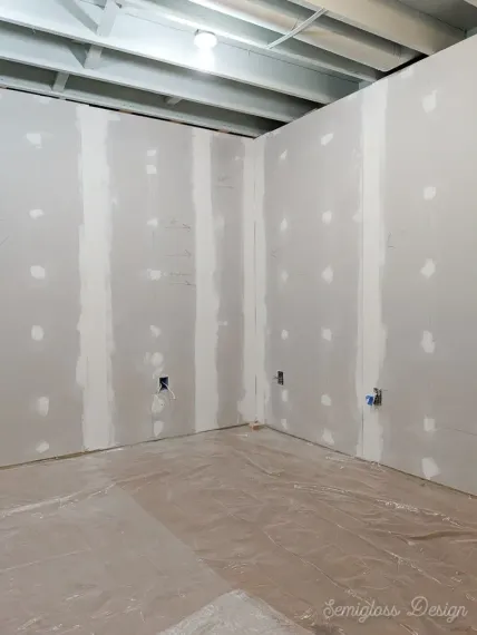 An empty room with drywall walls and a plastic sheet on the floor.