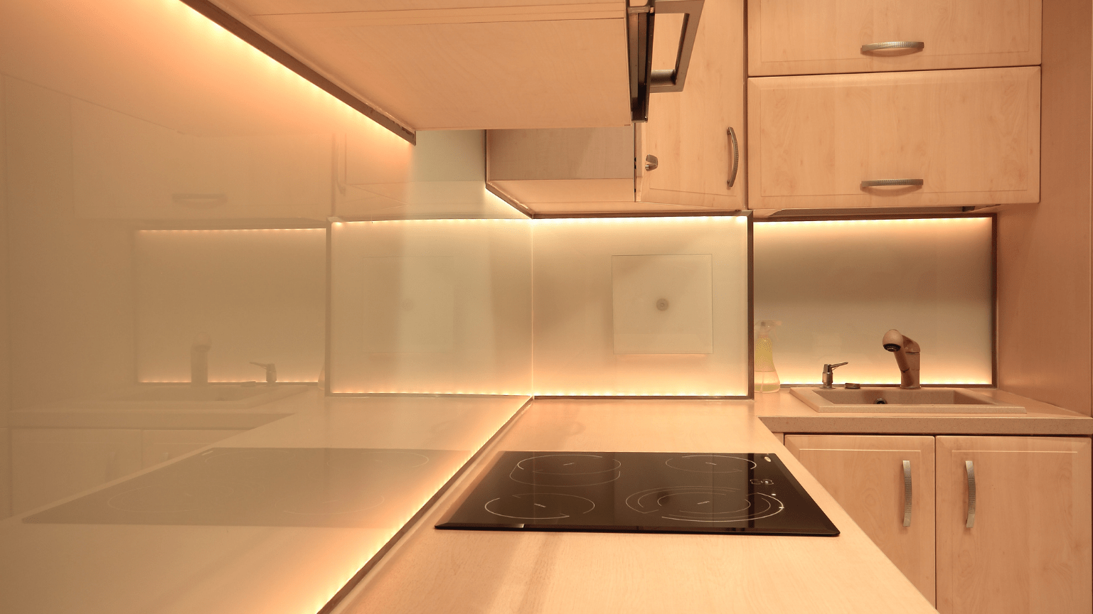 Modern kitchen with cream-colored cabinets and countertops, black cooktop, and warm under-cabinet lighting — Intolec Electrical In Tweed Heads, NSW