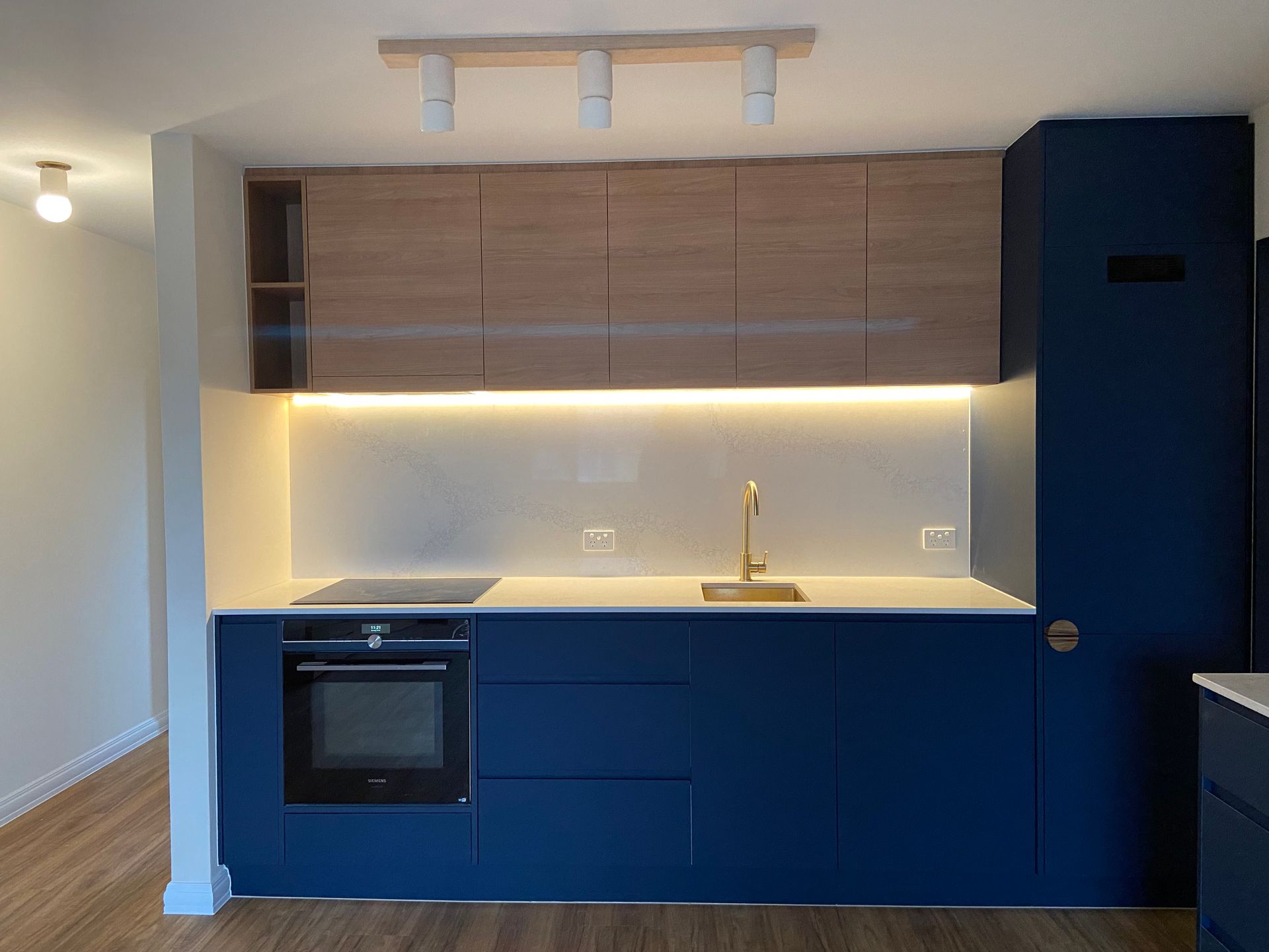 Modern kitchen with blue cabinets, wood upper cabinets, gold faucet, and under-cabinet lighting.