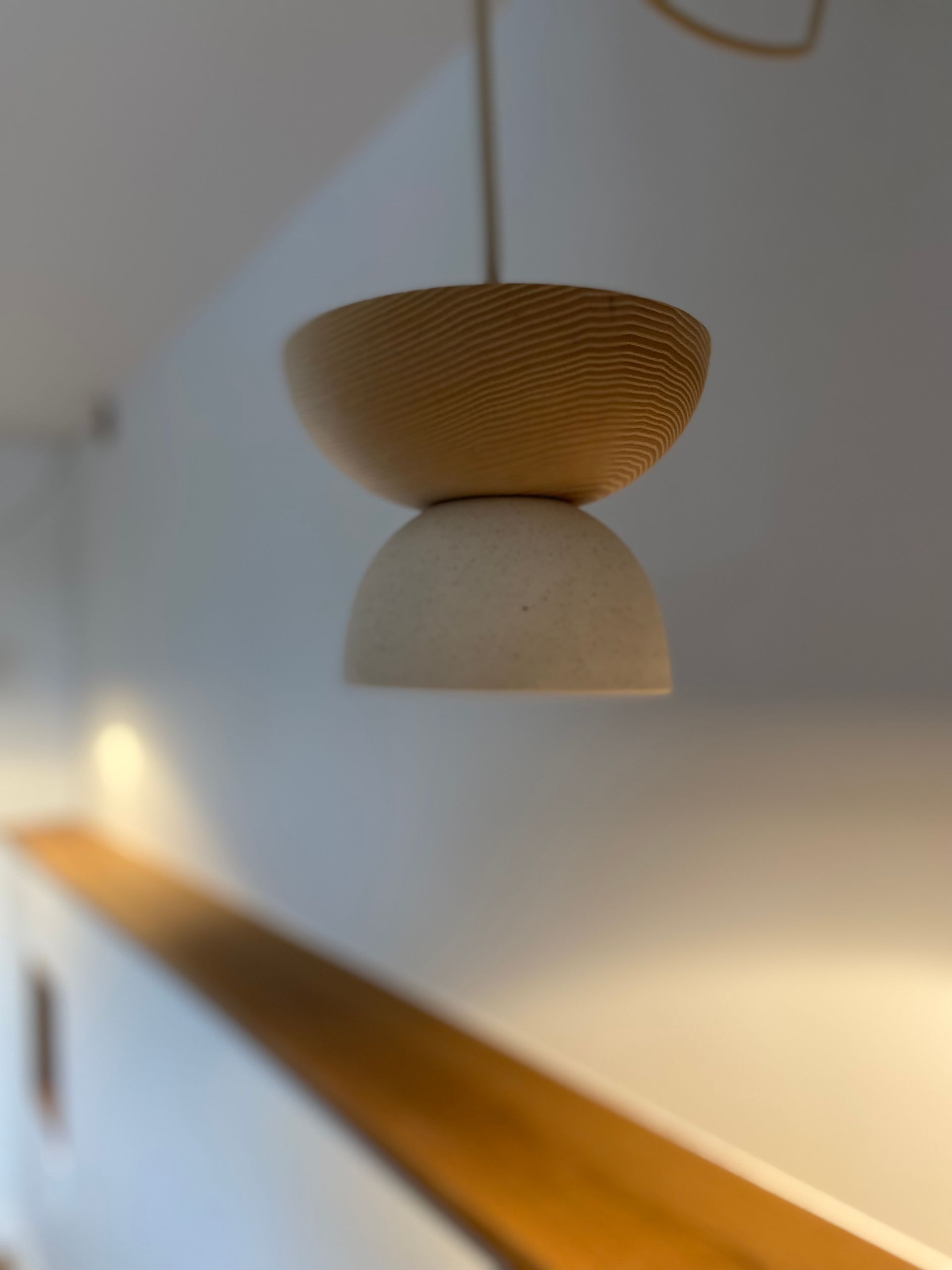 Modern, two-toned light fixture, hanging. Upper section textured wood, lower section smooth white. Soft focus background.