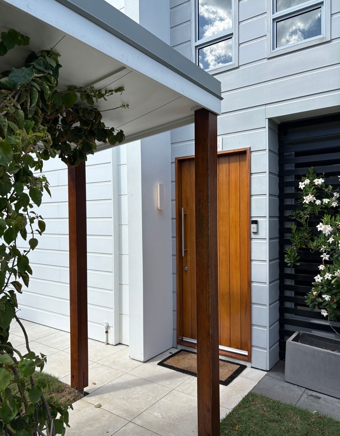 Wooden door under a white porch with brown support beams and light gray exterior.