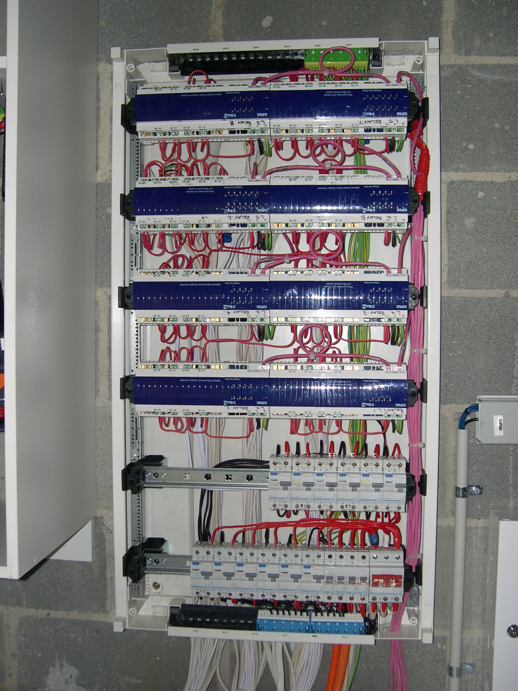 Electrical panel with organized wiring and circuit breakers, installed on a concrete block wall.