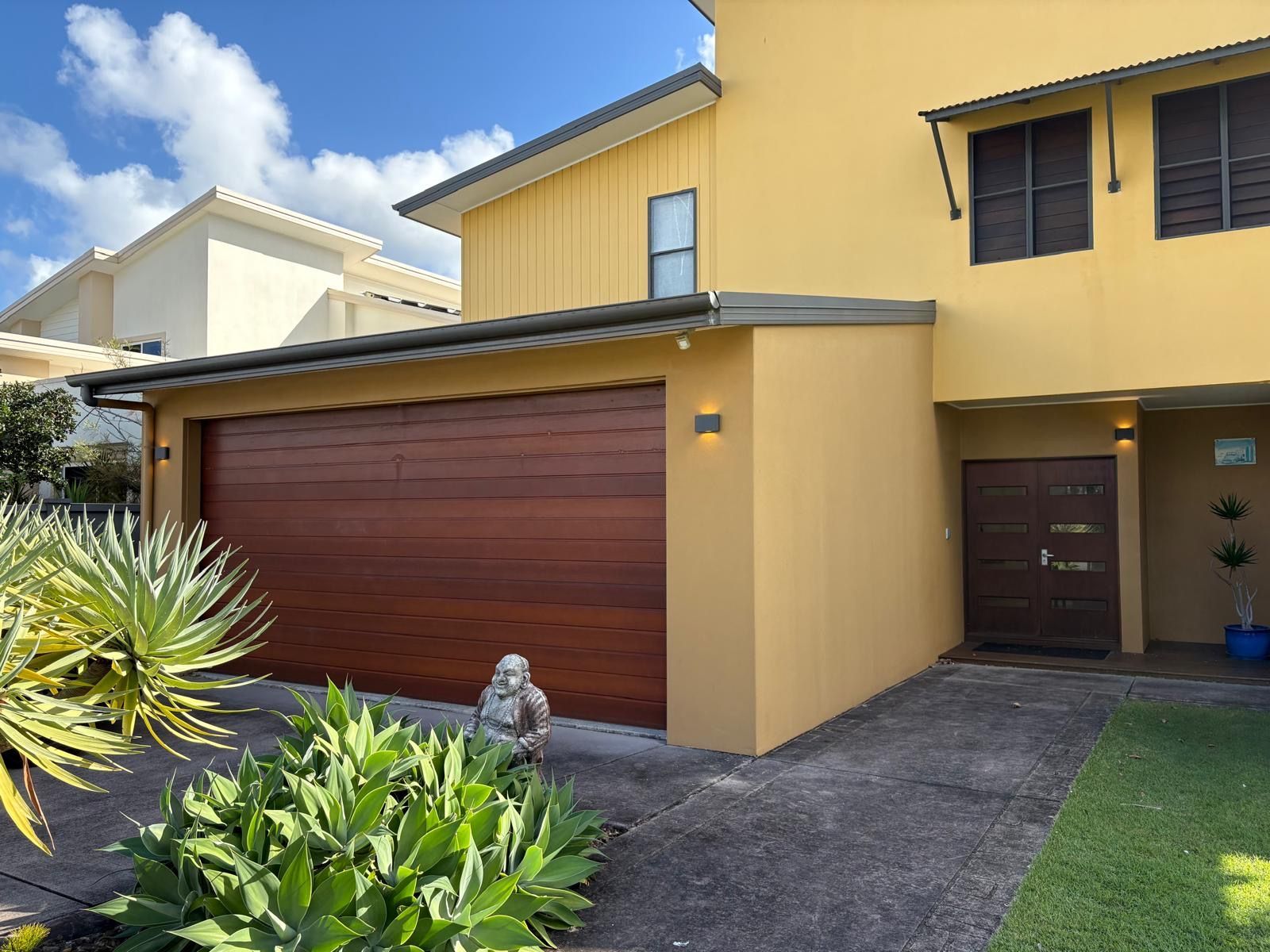 Yellow House With Brown Garage Door, Front Door, and Green Shrubs — Intolec Electrical in Tweed Heads, NSW