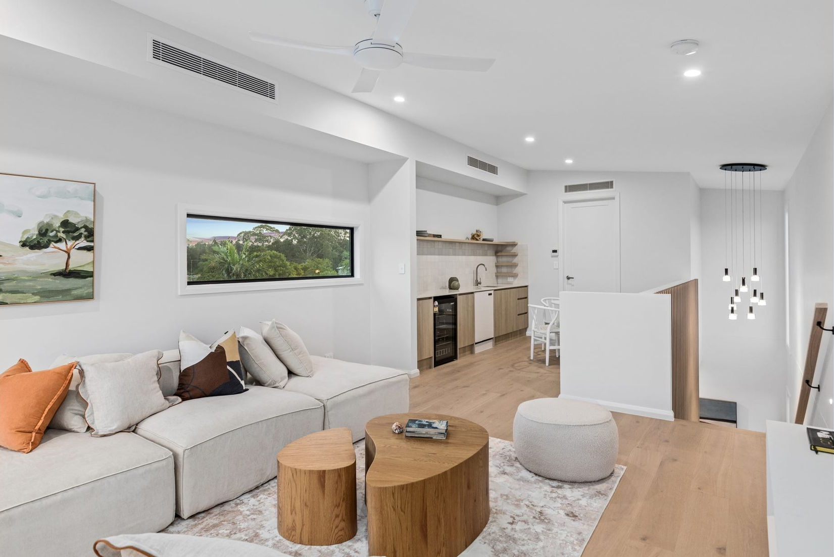 Spacious living room with hardwood floors, kitchen, and a large rug. Windows offer a view of greenery. — Intolec Electrical In Tweed Heads, NSW
